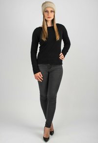 Maglione nero a maglia, jeans scuri e scarpe con tacco nere. Il modello indossa un berretto di maglia beige, caratterizzato da un motivo testurizzato.