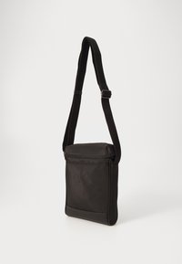 Juodas korsetas neštis, pagamintas iš nailono, su užtrauktuko uždarymu, reguliuojamu dirželiu ir elegantiška stačiakampio forma su minimaliai detalių.