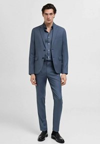 Slim-fit modra suknja, izdelana iz gladkega materiala, z enojnim zapenjanjem in hlačami ravnega kroja. V kompletu z ujemajočo srajco in črnimi čevlji.