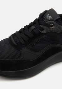 Black sneakers with a mesh and suede upper, featuring a textured panel, a rubber sole, and logo detail on the tongue.