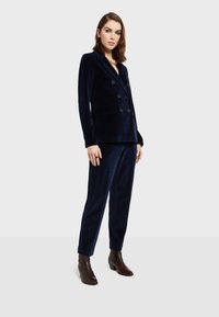 Námornícky sametový blejzer s dvojitým zapínaním, klopami a vreckami, skombinovaný s ladnými nohavicami a hnedými topánkami na podpätku.