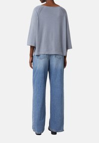 Lichtgrijze gebreide top met een ruime ronde hals en verlaagde schouders, gecombineerd met hooggeknipte, wijde blauwe jeans. Effen stof, zonder patronen.