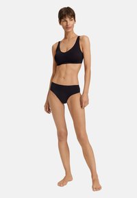 Černý bikinový set z jemného, lehkého materiálu. Halenka má kulatý výstřih a široká ramínka, zatímco kalhotky mají nízký střih.