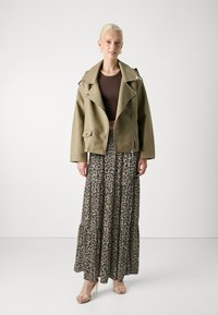 Maslinasto zelena motorkarska jakna sa srebrnim detaljima, smeđi kratki top i višeslojna maxi suknja s leopard uzorkom. Prozirne sandale s potpeticama zaokružuju outfit.