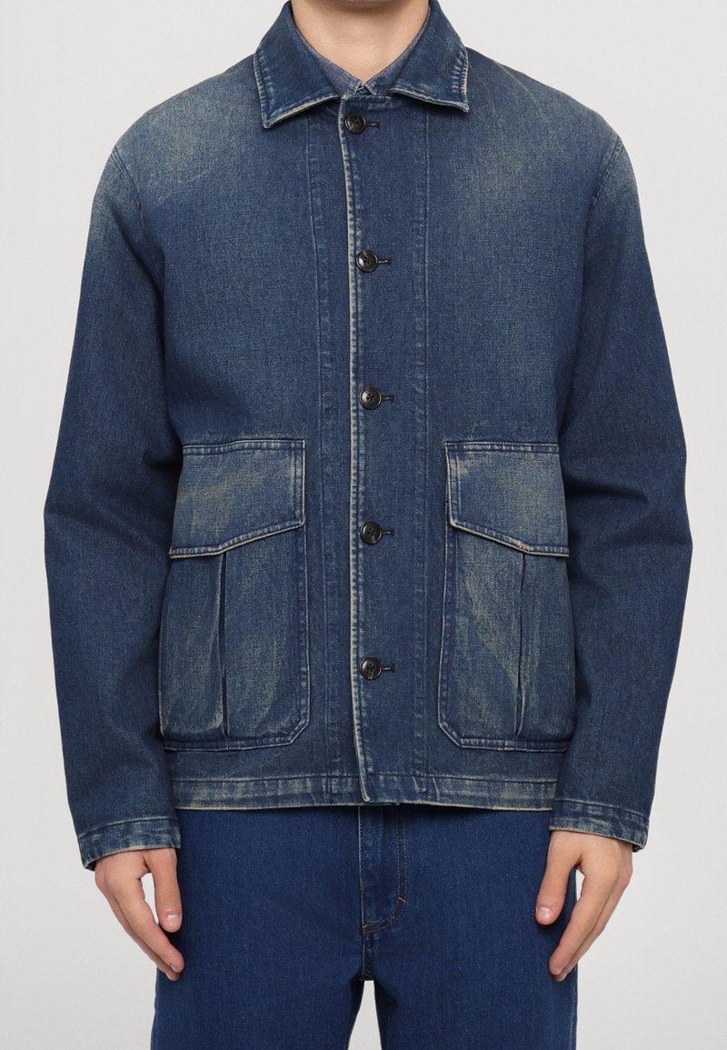 Homme portant une veste en denim bleue boutonnée avec deux grandes poches à rabat à l'avant et des détails délavés, associée à un jean bleu.
