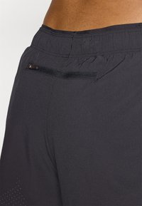 Black athletic shorts with a textured fabric, featuring an elastic waistband and a small zippered pocket on the back. Light perforations present.