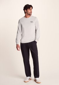 Light gray long-sleeve shirt with logo, paired with dark pants and white sneakers with black stripes. Comfortable fit and casual design.