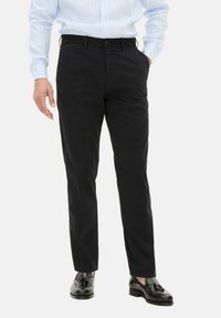 Chino in cotone blu navy con vestibilità dritta, dotato di tasche laterali e chiusura a bottone. Indossati con scarpe in pelle nere.