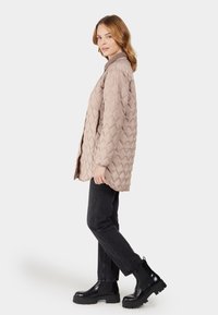 Lichtbeige gewatteerde jas met een V-hals en lange mouwen, gecombineerd met zwarte jeans en stevige zwarte laarzen. Eenvoudig, textuur ontwerp.