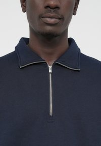 Sudadera de cremallera en azul marino con cuello alzado, confeccionada en suave algodón, que cuenta con una cremallera plateada y textura acanalada en el cuello.