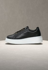 Μαύρο δερμάτινο αθλητικό παπούτσι χαμηλού τύπου με χρυσά μεταλλικά περβάζια, λευκή παχιά σόλα και το λογότυπο "Love Moschino" ανάγλυφο στο πλάι.