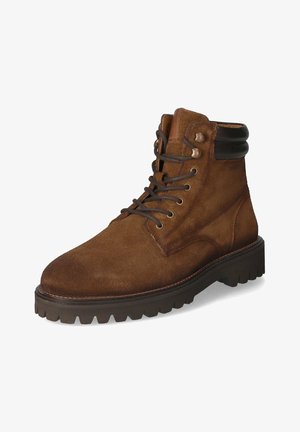 Stivale alla caviglia in suede marrone con accenti in pelle nera, punta rotonda e design con lacci. Presenta una suola robusta e testurizzata per una migliore aderenza.