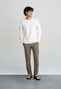 Valge pika varrukaga särk, millele on sobitatud pruunid mustriga püksid ja mustad loafersid valgete rihmadega. Minimalistlik, sobiv disain.