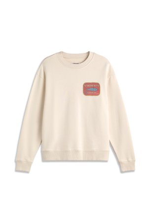 Sweatshirt beige à manches longues avec poignets et ourlet côtelés, présentant un petit graphique de boîte de sardines rouge et jaune sur le côté gauche de la poitrine.