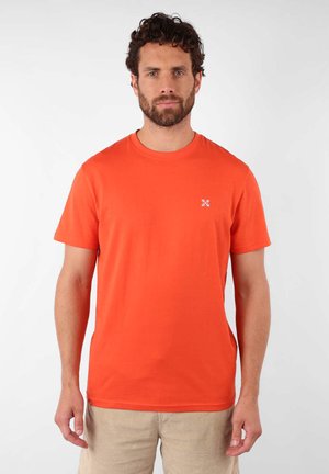 T-shirt en coton orange à manches courtes avec col rond et un petit graphisme blanc sur la poitrine gauche. Texture lisse, coupe décontractée.