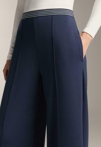 Námornícke široké nohavice s textúrovanou tkaninou, so bočnými vreckami a pruhovaným pásom v odtieňoch modrej a bielej.