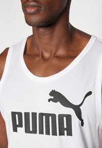 Biely tielko s veľkým čiernym logom "PUMA" a grafikou skáčucej pantery, vyrobené z jemnej bavlnenej tkaniny s klasickým strihom.