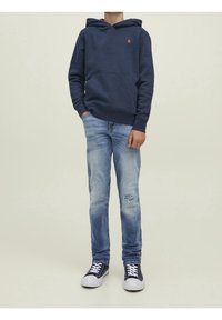 Námořnický modrý fleecový svetr s přední kapsou, kombinovaný se světle modrými roztrhanými džíny a námořnickými teniskami s bílou podrážkou.