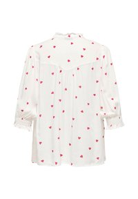 Blusa blanca con mangas cortas y abullonadas, con un escote con volantes y patrones de corazones rosas dispersos. Yugo trasero con ligeros fruncidos.