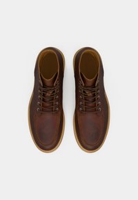 Une paire de bottes en cuir brun lacées avec des semelles beige clair, vues de dessus sur un fond blanc.
