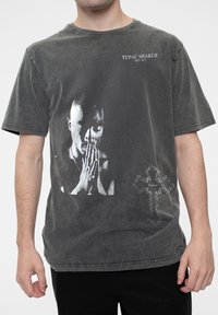 Gray graphic t-shirt featuring a black and white image of Tupac Shakur praying, with a cross design and text reading “TUPAC SHAKUR.”