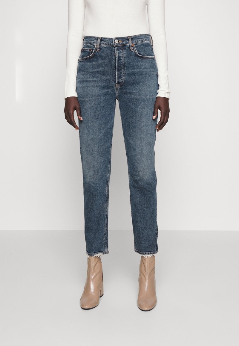 Jean droit bleu foncé avec ourlet effiloché, poches avant et fermeture à boutons classique, stylé avec des bottines beiges.