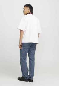 Hvit oversized t-skjorte, denimbukser, svarte fottøy. Rød og hvit mønstret bandana rundt halsen, minimalistisk design.