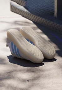 Vita sneakers med ljusblå ränder, gummisulor, strukturerade mönster och en låg profil. Accenter inkluderar en liten röd detalj nära hälen.