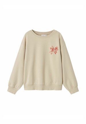 Beżowa bluza z długim rękawem z prążkowanymi mankietami i dołem, z małą czerwoną kokardką na lewej piersi.