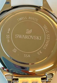 Swarovski-Uhrenrücken, Goldton-Edelstahl, graviert mit "SWAROVSKI", "Swiss Made" und einer Wasserdichtigkeit von 50 m. Glatte Oberflächenbeschaffenheit.