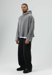 Grijze oversized hoodie met een capuchon, voorzien van brede mouwen. Gecombineerd met losse zwarte jeans en zwarte chunky schoenen met roze veters.