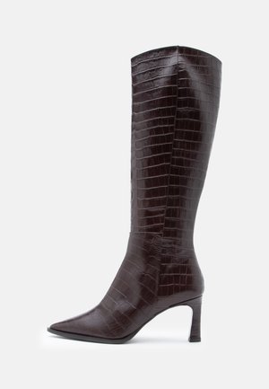 Bottes brunes à talons, hauteur genou, en cuir à motif crocodile avec un bout pointu et un talon fin, présentant une texture lisse.