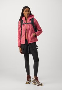 Lightweight, pink waterproof jacket with a hood, black cargo shorts, black leggings, and brown hiking shoes with a textured sole.