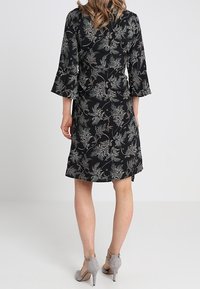 Schwarzes Kleid mit floralem Muster, ausgestelltem Ärmel, knielangem Schnitt, leichtem Stoff und kombiniert mit grauen High Heels.