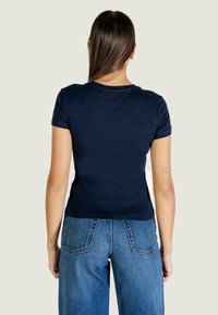 Tmavě modré bavlněné tričko s krátkými rukávy, kulatým výstřihem a mírně přizpůsobeným střihem, v kombinaci s modrými džíny s vysokým pasem.