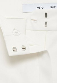 Biały pas z dwoma metalowymi zapięciami na hak i oczko, przezroczystym guzikiem oraz białą etykietą rozmiaru oznaczoną jako MNG.