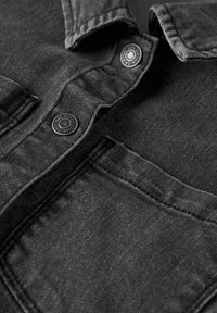 Camisa de denim negra con cuello abotonado, tela texturizada y bolsillos en la parte delantera. Presenta botones redondos negros y detalles de costuras visibles.