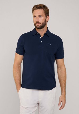 Dunkelblaues Baumwoll-Polohemd mit Kragen, zwei Knöpfen und einer Brusttasche mit kleinem Logo. Tragen Sie es mit hell gestreiften Hosen.