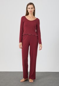 Burgundy pyjamaset med långa ärmar och utsvängda byxor, med en kort topp som har volangnederdel och ribbad textur. Mjuk tyg.