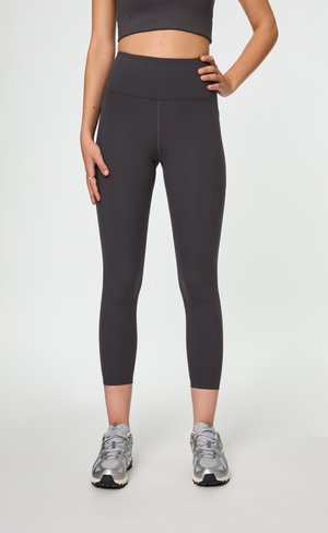 Leggings mi-hauts, coupés dans un tissu gris foncé avec une texture lisse ; associés à des chaussures de sport gris clair.
