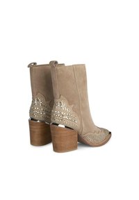 Buciki za kostkę w jasnym beżowym zamszu z wyciętym wzorem na obcasie, drewnianym blokowym obcasem oraz otwartym noskiem. Posiada akcenty dekoracyjne.