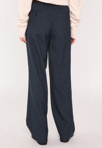Pantalon large en laine bleu foncé à fines rayures verticales, doté de poches arrière et d'une ceinture. Texture douce avec une légère brillance.