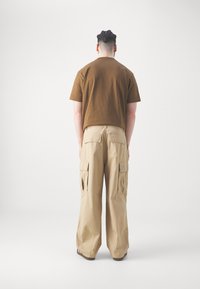 Brun kortærmet T-shirt parret med løse, beige cargo bukser med flere sidelommer og et patch på baglommen.