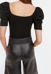 Top nero lavorato a maglia con maniche corte a palloncino, caratterizzato da un collo a barca. Abbinato a pantaloni shorts in pelle nera a vita alta.