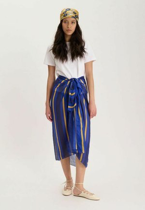 Femme aux cheveux longs portant un t-shirt blanc, une jupe portefeuille rayée bleue et jaune, un foulard assorti et des chaussures plates crème à lacets.