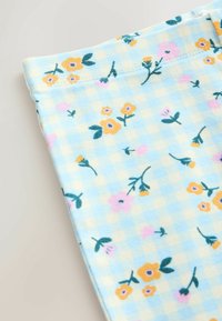 Tessuto azzurro chiaro con motivo a quadri, decorato con disegni floreali sparsi in giallo, rosa e verde. Texture morbida, bordi cuciti.