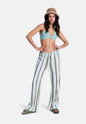 Svetlomodrý vrchný diel plaviek so vzorom v kombinácii s voľnými bielymi nohavicami so zelenými pruhmi. Modelka má na hlave slamák a zelené sandále.