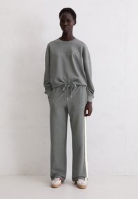 Szara bluza i dopasowane dresy z miękkiego materiału. Góra z wyciśniętymi detalami logo; spodnie mają kontrastowe paski po bokach.