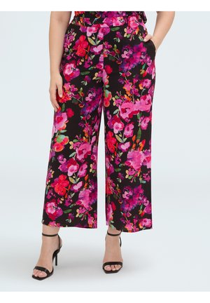 Woman wearing black wide-leg pants with bright pink, red, and purple floral print, paired with black ankle-strap high heels.
