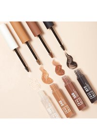 Four eyebrow products in various shades: white, light brown, dark brown, and black, with corresponding cream swatches on a light background.